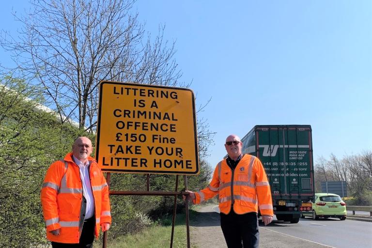 Cllr Barry Hunt and Robert Hoof an the side of A66 next to a sign asking drivers not to throw their litter on the road