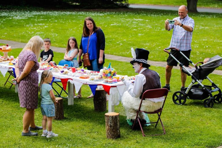 Image of the Mad Hatter at Tea Party Kirkleatham Museum, entertaining the children and parents at the long table filled with food and sweets..