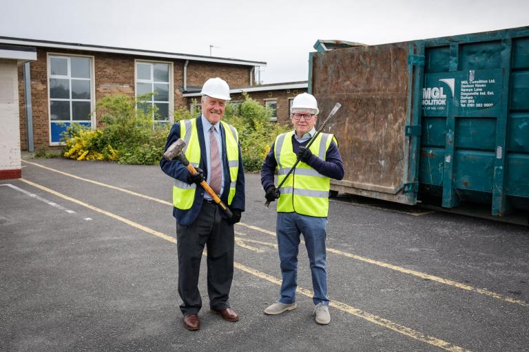 Image of Councillor Steve Kay and Councillor Chris Gallacher, dressed in safety equipment and holding construction tools, in front of the Eston swimming pool 