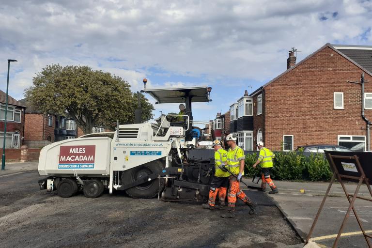 Workers operating an asphalt paver to resurface the Stirling road
