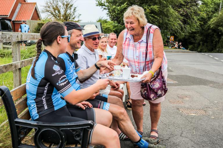 Crowds sitting on a bench and eating snacks at the Road Race.