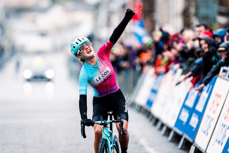 Alice Towers winning the women's race last year wearing a blue and pink jersey. Alice's arm is raised in celebration.