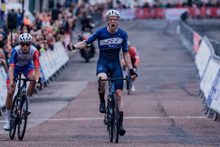 Image of a cyclist wearing a blue jersey celebrating winning a race. 