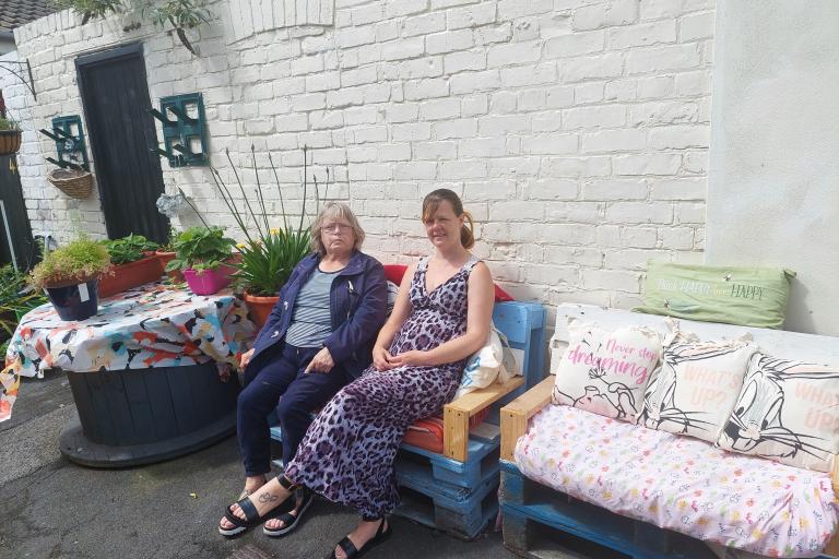 Image showing two women seating on the pallet benches in a back garden. 