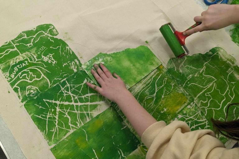 artwork in progress. A young woman paints a large canvas with green paint.