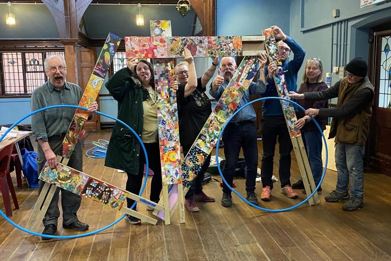 Artists holding a huge artwork in the form of a bike made out of different paintings.