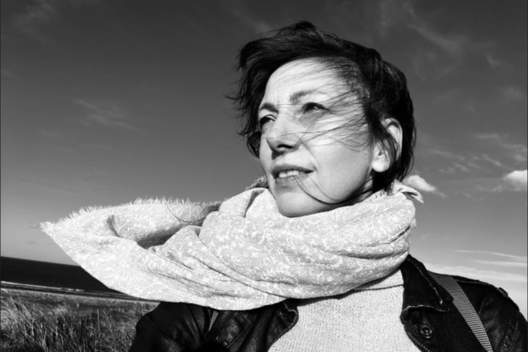 White and black picture of a woman wearing a scarf around her neck and looking in the distance.