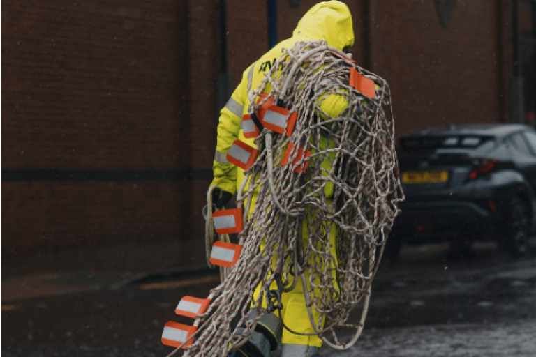 Picture from the RNLI exhibition of a RNLI volunteer dressed in yellow equipment caring many fishing ropes on the street.