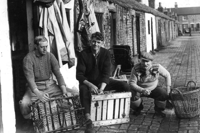Black and White picture of three fisherman sitting in front of their house.