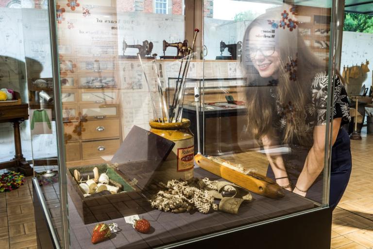 Woman admiring an exhibit featuring an antique sewing kit inside a museum.