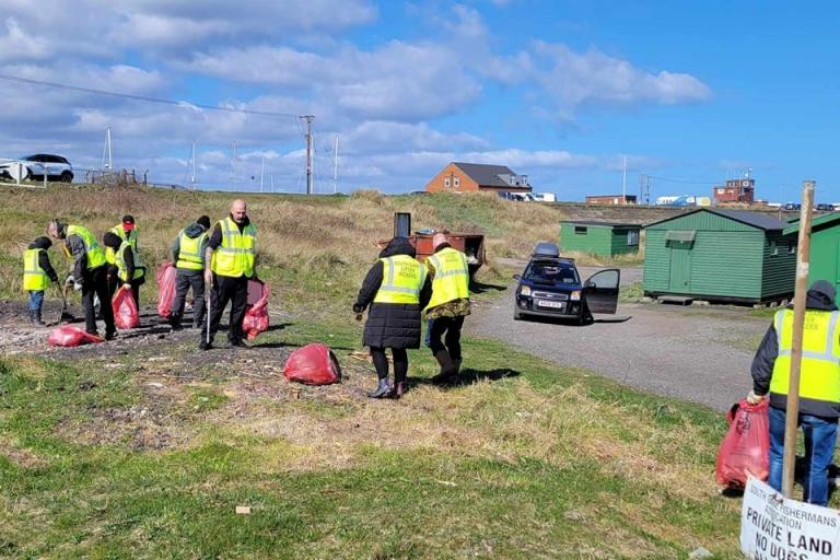 Image of litter pickers at south gare. They are wearing yellow high vis and collecting rubbish in red bags.