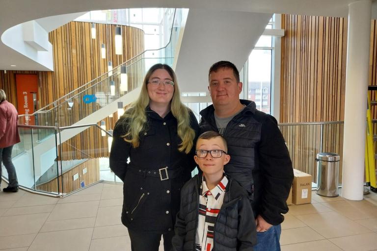 a woman, a man and their boy dressed in winter coats smiling to the camera.