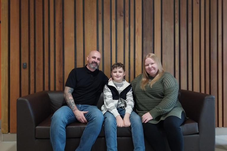 A man and a woman sitting on a couch with their boy in the middle.