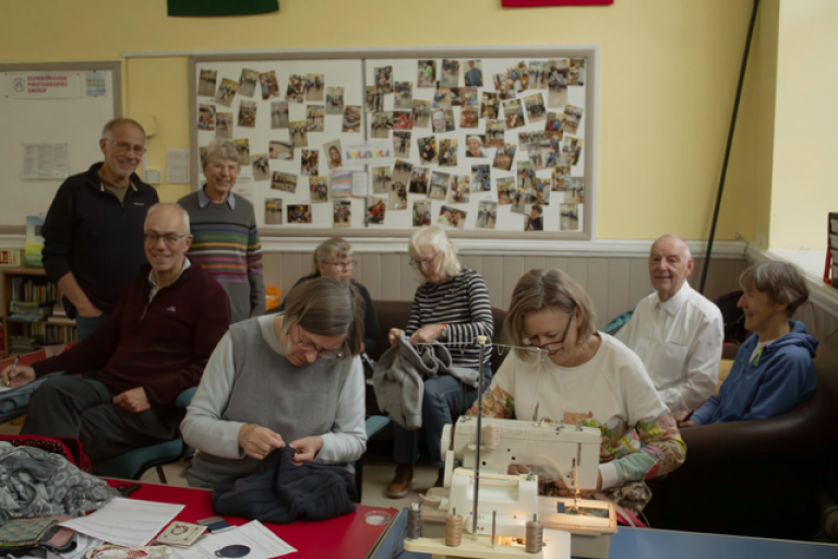 Image of a volunteer group. There is a mix of men and women undertaking a craft class. There is a whiteboard in the background with images of projects they have completed.