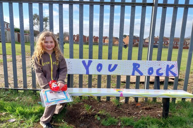 A girl sitting on a colourful bench that reads You Rock