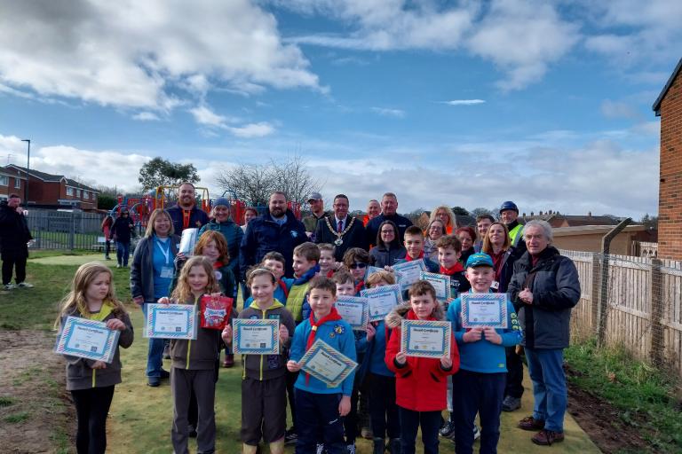 A group of children holding certificates at the front with adults behind them standing in a play area