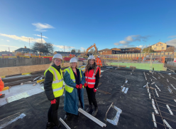 Image of three women in a building site wearing white helmets and hi-viz jackets.