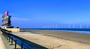 Picture of the Redcar Beach on a sunny day with blue sky, the Beacon, the sea and windmills in the background.