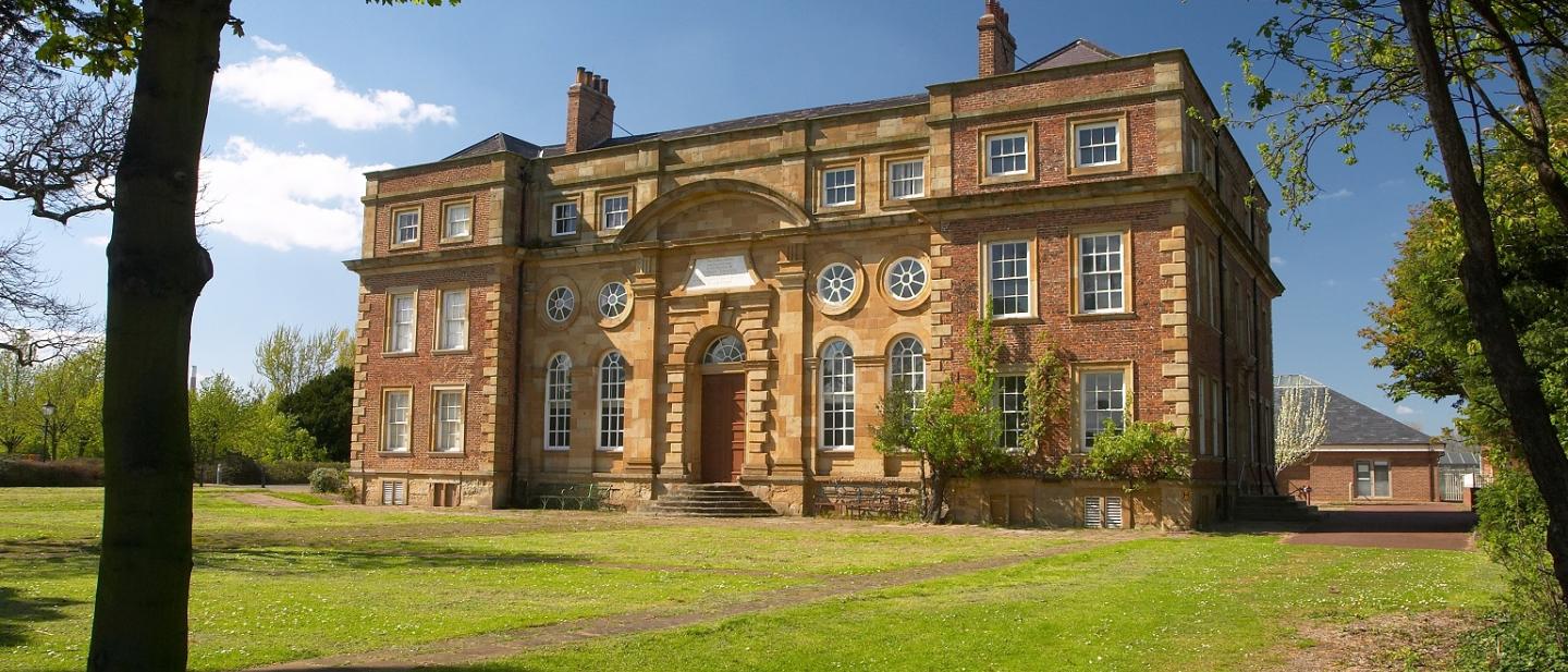 Image of Kirkleatham Museum on a summer day. The building is made up of light yellow and brown bricks.