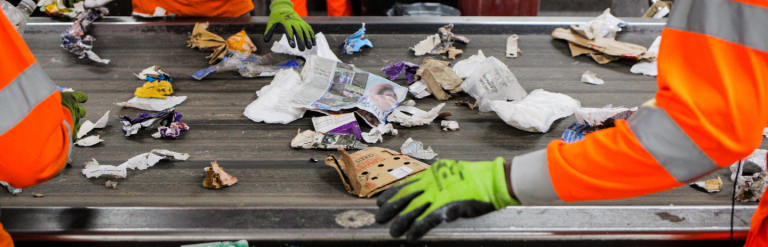 Image showing recycling being sorted on a conveyor belt by staff wearing orange hi-vis jackets and yellow gloves.